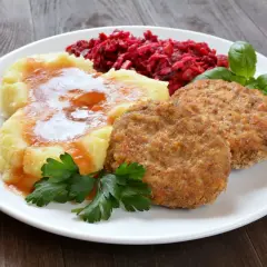Dwa złociste mielone z piekarnika, podane z purée ziemniaczanym polanym sosem, surówką z buraków i listkami bazylii.