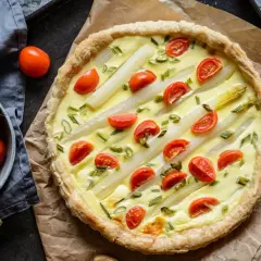 Pyszna tarta ze szparagami i pomidorkami koktajlowymi, udekorowana szczypiorkiem. Idealna na wiosenny obiad.