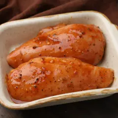 Dwie soczyste piersi z kurczaka w marynacie z przyprawami, gotowe do pieczenia.