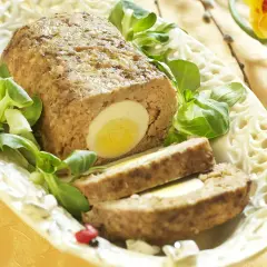Pyszna pieczeń z mięsa mielonego z jajkiem w środku, udekorowana sałatką i wiosennymi kwiatami.