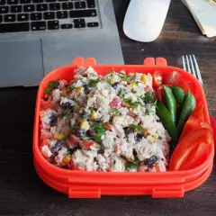 Pyszna sałatka z ryżem, kurczakiem, kukurydzą i fasolą w pomarańczowym pudełku. Obok pomidorki, groszek i papryka. Idealny lunch do pracy.