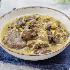 Pyszna wątróbka drobiowa z cebulką w sosie, podana w misce na granatowej serwetce. Obok widoczna miska z kaszą.