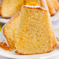 Puszysta babka z mascarpone, oprószona cukrem pudrem i ozdobiona skórką pomarańczową, na talerzyku z tulipanami.