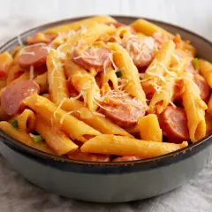 Penne z sosem pomidorowym i plasterkami kiełbasy, posypane parmezanem. Pyszny makaron z kiełbasą w misce.