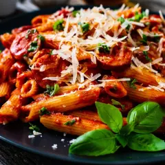 Penne z krewetkami w sosie pomidorowym, posypane parmezanem i udekorowane bazylią.