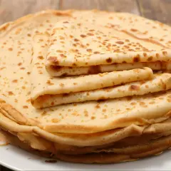 Stos cienkich, lekko zarumienionych naleśników bez jajek, ułożonych na białym talerzu. Idealne na śniadanie lub deser.