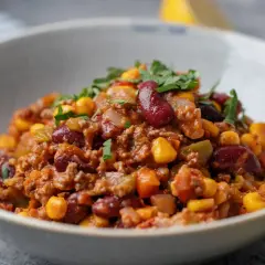 Miseczka pełna aromatycznego chili con carne z fasolą, kukurydzą i mielonym mięsem, posypana świeżą natką pietruszki.