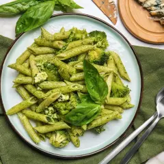 Penne z brokułami i serem gorgonzola w sosie pesto, udekorowane listkami bazylii. Idealne danie dla miłośników makaronu.