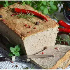 Pyszny pasztet mieszany drobiowo-wieprzowy, udekorowany papryczką chili i ziołami, gotowy do podania na kromkach chleba.