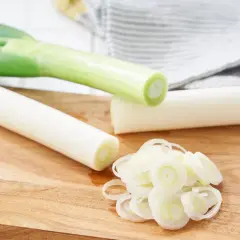 Na drewnianej desce leżą pory, część pokrojona w krążki, gotowa na pyszną surówkę z pora.