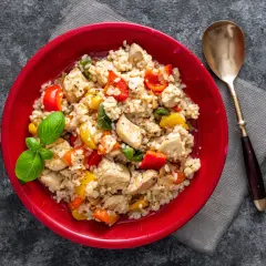 Pyszne risotto z kurczakiem, kolorową papryką i świeżą bazylią, podane w czerwonej misce.