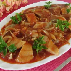 Pyszne śledzie po cygańsku w sosie pomidorowym z cebulką, udekorowane natką pietruszki.