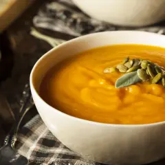 Aksamitna zupa z dyni, udekorowana pestkami dyni i listkiem szałwii, podana z chrupiącym pieczywem.