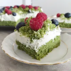 Zielony biszkopt przełożony kremem z mascarpone, ozdobiony malinami i borówkami. Pyszne ciasto leśny mech z mascarpone.