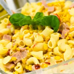 Pyszna sałatka z makaronem, kukurydzą i kawałkami szynki, udekorowana listkiem bazylii. Idealna na letnie dni.
