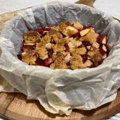 Pyszne owoce pod kruszonką, zapieczone w papierze do pieczenia, czekają na talerzu.