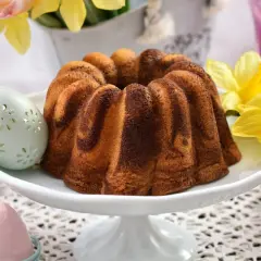 Wilgotna babka wielkanocna dwukolorowa, ozdobiona wielkanocnymi pisankami i żółtymi żonkilami, zapowiada wiosenne święta.