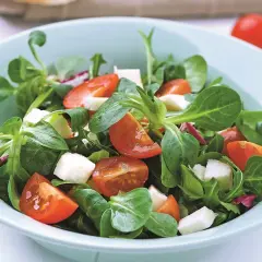 Świeża sałatka z roszponką, pomidorkami koktajlowymi i kostkami sera mozzarella w jasnoniebieskiej misce.