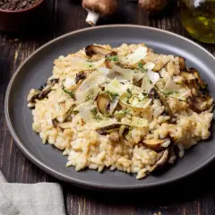 Aksamitne risotto z pieczarkami, posypane parmezanem i świeżym tymiankiem, prezentuje się apetycznie na ciemnym talerzu.