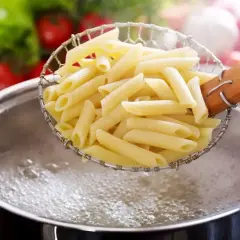 Penne makaron w cedzaku nad garnkiem z gotującą się wodą. Idealny sposób, jak ugotować makaron.