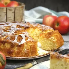 Puszyste ciasto na oleju z jabłkami, posypane cukrem pudrem. Obok jabłka i nóż.