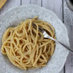 Pyszne cacio e pepe na talerzu z ozdobnym wzorem. Widok z góry na makaron spaghetti z serem i pieprzem, z widelcem w środku.