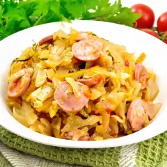 Pyszny bigos z młodej kapusty z kiełbasą, podany na białym talerzu, ozdobiony zieloną natką i pomidorkami.
