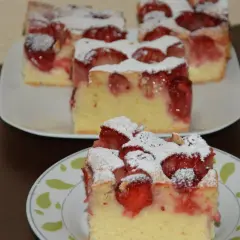 Pyszne ciasto ucierane z truskawkami, posypane cukrem pudrem, prezentuje się apetycznie na talerzykach.