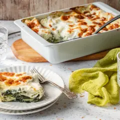 Pyszne lasagne ze szpinakiem, zapieczone na złoto, podane na talerzu obok szklanki wody z cytryną.
