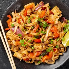 Pyszny pad thai z kurczakiem, makaronem ryżowym, warzywami i limonką.