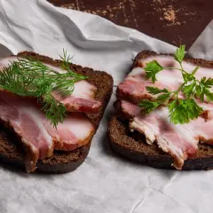 Dwa kanapki z ciemnego chleba z plastrami boczku i ziołami. Idealne, gdy zastanawiasz się, jak upiec boczek.