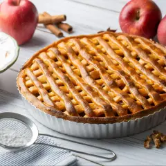 Złocista tarta z jabłkami z kratką z ciasta, jabłka, cynamon i orzechy na drewnianym stole.