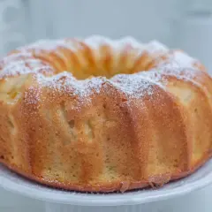 Puszysta babka na oleju, oprószona cukrem pudrem, prezentuje się apetycznie na białej paterze. Idealna na niedzielne popołudnie.