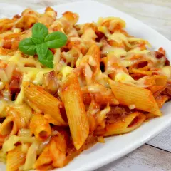 Penne z sosem pomidorowym i kawałkami pikantnego chorizo, zapieczone pod ciągnącym się serem. Udekorowane listkiem bazylii.
