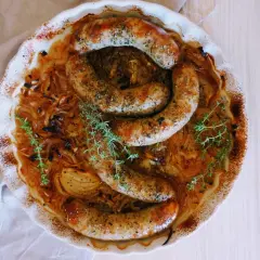 Złocista biała kiełbasa w piwie, zapiekana z cebulą i tymiankiem, prezentuje się apetycznie w ceramicznym naczyniu.