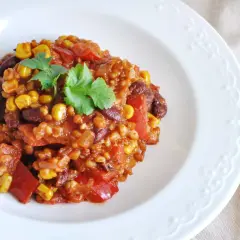 Kolorowe kaszotto z warzywami: kukurydza, fasola, papryka i pomidory, udekorowane natką pietruszki.
