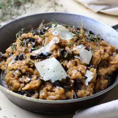 Aksamitne risotto z grzybami, udekorowane płatkami parmezanu i gałązkami tymianku, podane w metalowej patelni.