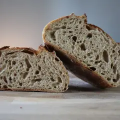 Chleb pszenno żytni na zakwasie, przekrojony na pół, prezentuje apetyczny, porowaty miąższ i chrupiącą skórkę.