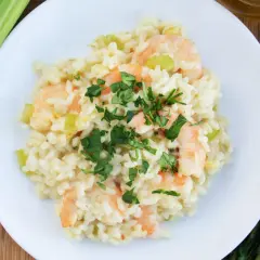 Pyszne risotto z krewetkami, ozdobione natką pietruszki, obok łodygi selera i butelka oliwy.