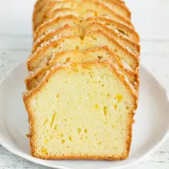 Pokrojona babka piaskowa cytrynowa z cukrową posypką, ułożona na białym talerzu.