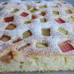 Puszyste ciasto jogurtowe z rabarbarem i kruszonką, posypane cukrem pudrem. Idealne na letnie popołudnie.
