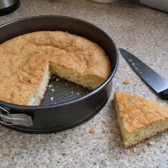 Puszysty biszkopt na tort w tortownicy, obok nóż i kawałek ciasta. Idealny do dalszego dekorowania.