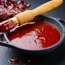 Pyszne żeberka w sosie bbq. Pędzel zanurzony w sosie, gotowy do posmarowania mięsa. Idealny sos bbq przepis na grilla.