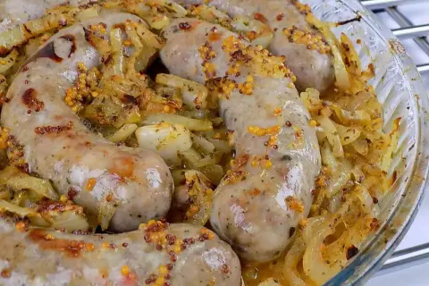 Pyszna biała kiełbasa pieczona w cebuli i musztardzie, z chrupiącymi ziarnami gorczycy. Aromatyczne danie w szklanej formie.