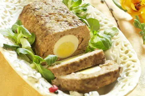 Pyszna pieczeń z mięsa mielonego z jajkiem w środku, udekorowana sałatką i wiosennymi kwiatami.