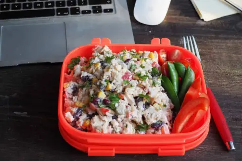 Pyszna sałatka z ryżem, kurczakiem, kukurydzą i fasolą w pomarańczowym pudełku. Obok pomidorki, groszek i papryka. Idealny lunch do pracy.