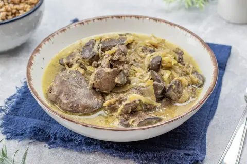 Pyszna wątróbka drobiowa z cebulką w sosie, podana w misce na granatowej serwetce. Obok widoczna miska z kaszą.