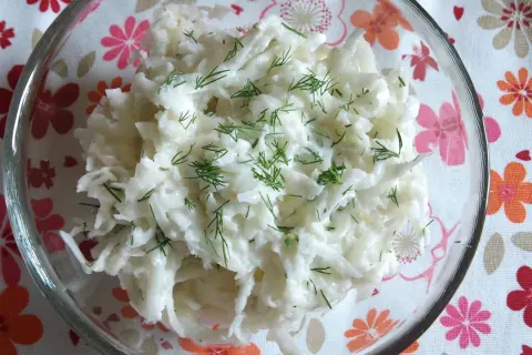 Pyszna surówka z białej rzodkwi, posypana świeżym koperkiem, w szklanej misce na kwiecistym obrusie.