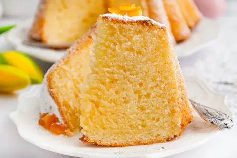 Puszysta babka z mascarpone, oprószona cukrem pudrem i ozdobiona skórką pomarańczową, na talerzyku z tulipanami.
