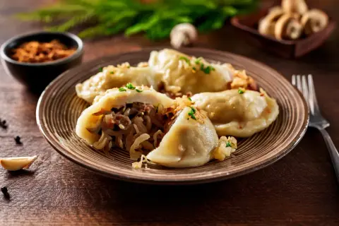 Pyszne pierogi z kapustą i grzybami, posypane szczypiorkiem, na talerzu z widelcem obok.